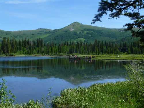 A serene lake surrounded by lush greenery and mountains, reflecting the landscape in calm waters.