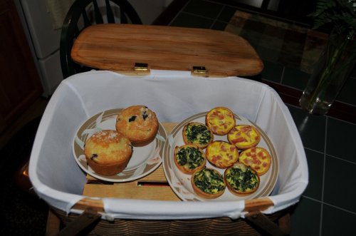 A picnic basket with two blueberry muffins and a plate of mini quiches with spinach and cheese.