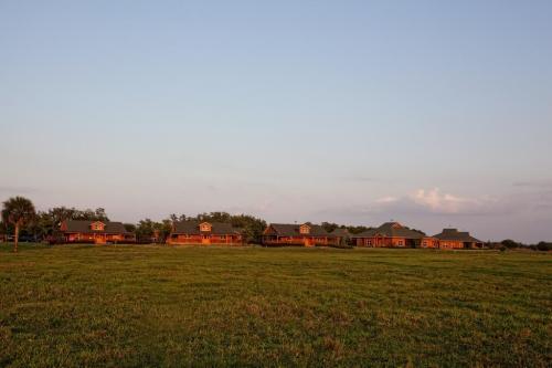A row of rustic houses sits against a clear sky, surrounded by green grass and trees in the background.