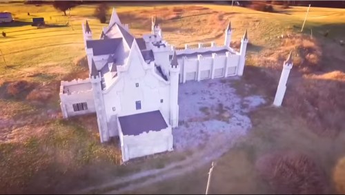Aerial view of a large, castle-like structure surrounded by open fields and a few trees.