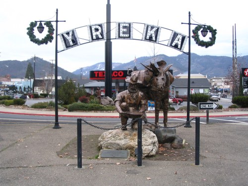 A statue of a miner and a horse under a sign reading "Yreka," with festive wreaths and mountains in the background.