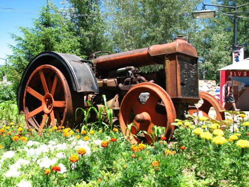 An old, rusty tractor surrounded by colorful flowers in a garden setting.