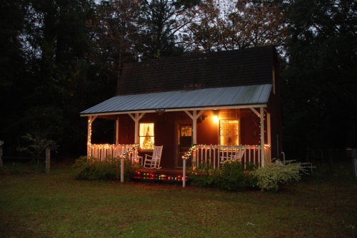 A cozy cabin decorated with colorful lights, surrounded by greenery, on a dark, serene evening.