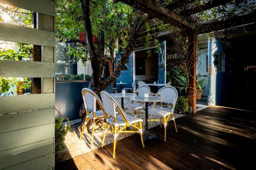 A cozy outdoor dining area with round tables and yellow chairs, surrounded by greenery and rustic decor.