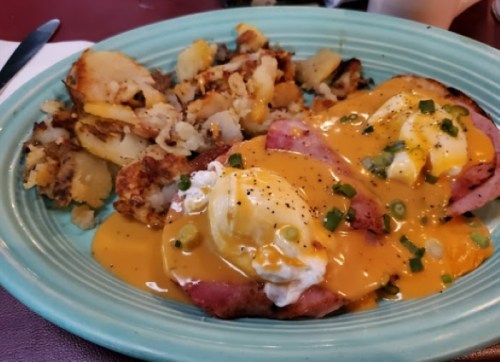 A plate of eggs Benedict with ham and hollandaise sauce, served with crispy hash browns on the side.