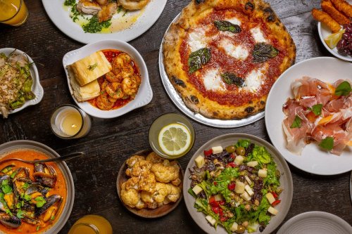 A spread of various dishes including pizza, shrimp, salad, and appetizers on a wooden table.