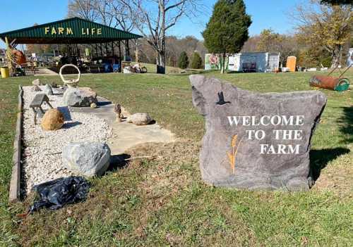 A large stone sign reading "Welcome to the Farm" in a grassy area with decorative rocks and a shelter in the background.