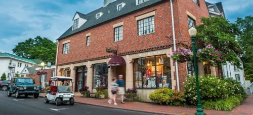 A brick building with large windows, featuring shops, surrounded by greenery and a golf cart on the street.
