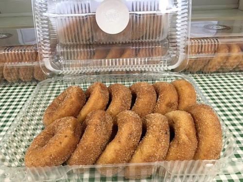 A clear container filled with freshly made, cinnamon-sugar coated donuts, arranged neatly on a checkered tablecloth.