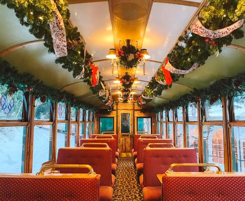 Interior of a festive train car, decorated with garlands and lights, featuring red upholstered seats and a cozy atmosphere.
