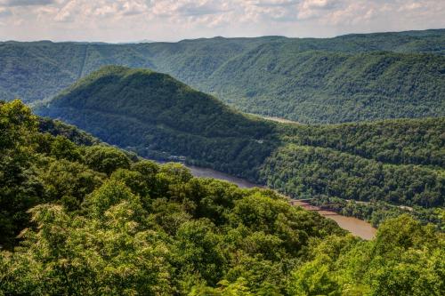 Lush green mountains and valleys surround a winding river under a partly cloudy sky.