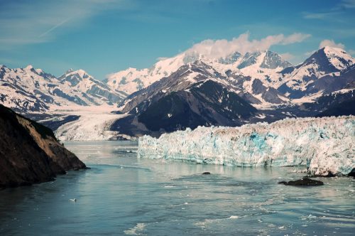 A stunning landscape featuring a glacier, mountains, and a calm river under a clear blue sky.