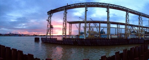 Panoramic view of a waterfront with industrial structures against a colorful sunset sky.