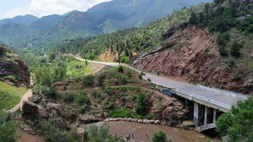 A scenic view of a winding road alongside a river, surrounded by mountains and lush greenery.