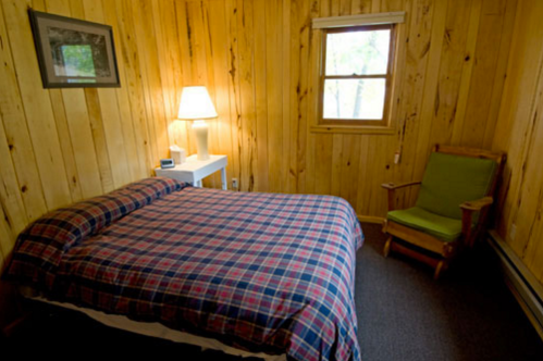Cozy wooden room with a plaid bedspread, a lamp, a window, and a green rocking chair.