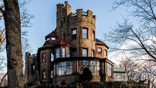 A large, stone castle with turrets and large windows, surrounded by bare trees against a clear blue sky.