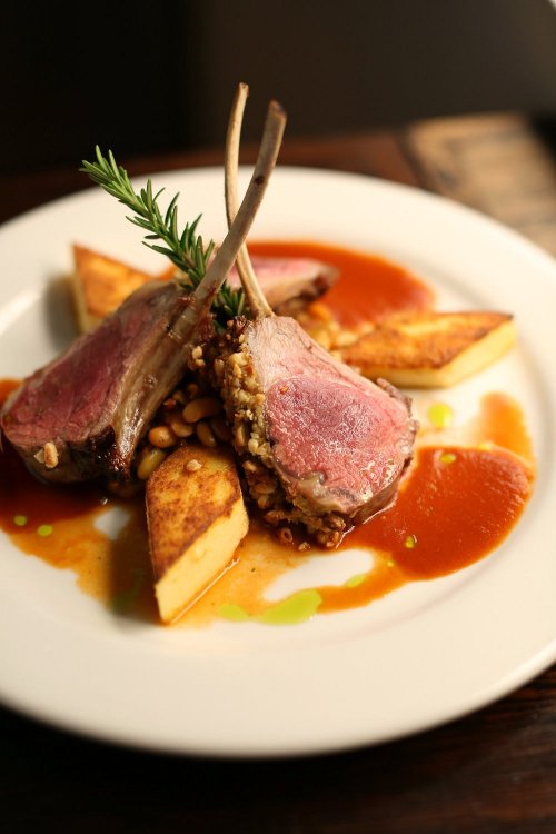 A plate of lamb chops with a crust, served with golden potato wedges and a rich sauce, garnished with a sprig of rosemary.