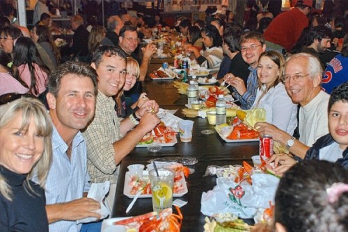 A group of people enjoying a meal together at a long table, smiling and sharing food in a lively setting.