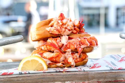 A towering lobster roll stacked high with fresh lobster meat, served with a lemon wedge on a wooden table.
