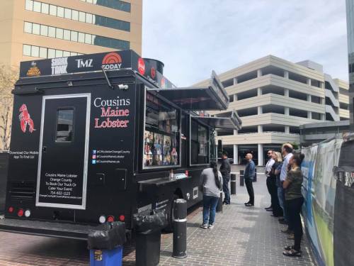 A food truck named "Cousins Maine Lobster" parked in a city area, with people lined up to order.
