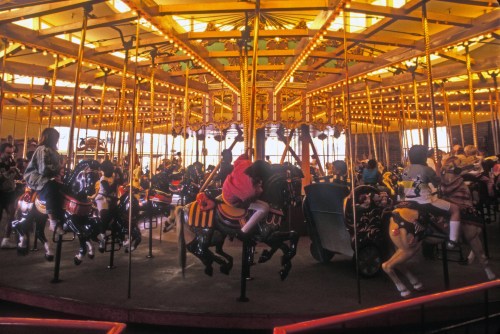 A colorful carousel with children riding horses, illuminated by warm lights in a festive atmosphere.