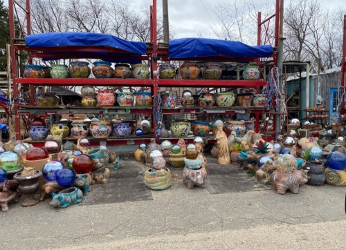 Colorful decorative pots and sculptures displayed on shelves and the ground at an outdoor market.