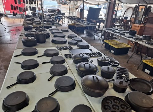 A variety of cast iron cookware displayed on tables under a tent at a market.