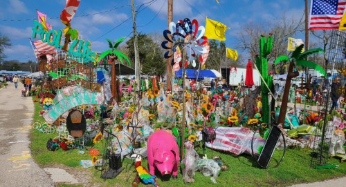 Colorful outdoor market display featuring various decorations, including flowers, flags, and a pink pig statue.