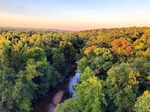 Aerial view of a winding river surrounded by lush green trees, with hints of autumn colors under a clear sky.
