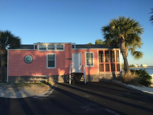 A pink beach house with palm trees, a front porch, and a clear blue sky in the background.