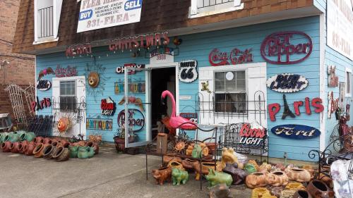A colorful storefront with various signs, a pink flamingo, and decorative pottery displayed outside.