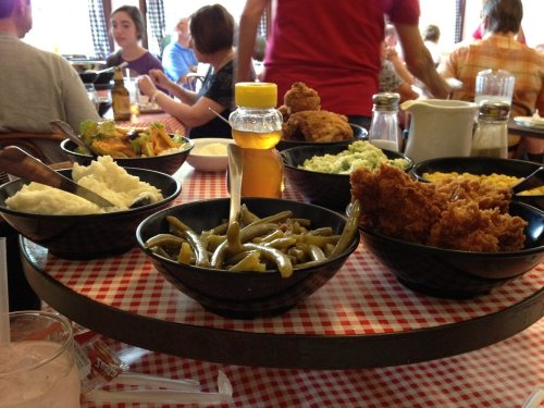 A table with bowls of fried chicken, green beans, mashed potatoes, coleslaw, and honey, set in a casual dining environment.