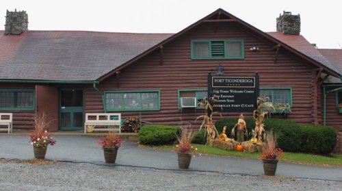 A rustic log cabin building with a sign, surrounded by flower pots and autumn decorations.