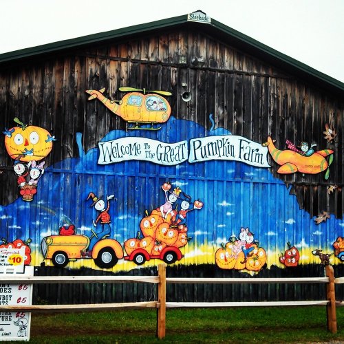 Colorful mural on a barn featuring cartoon characters, pumpkins, and a welcome sign for "The Great Pumpkin Farm."