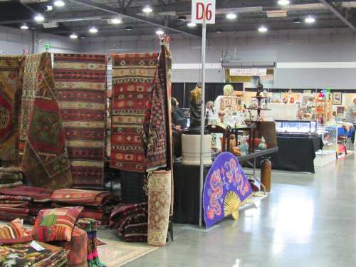 A vibrant market scene featuring colorful rugs and various decorative items in a spacious exhibition hall.