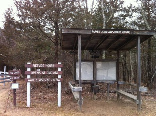 Signage at Parker Woodland Wildlife Refuge, detailing hours and rules, with a wooden shelter in a natural setting.