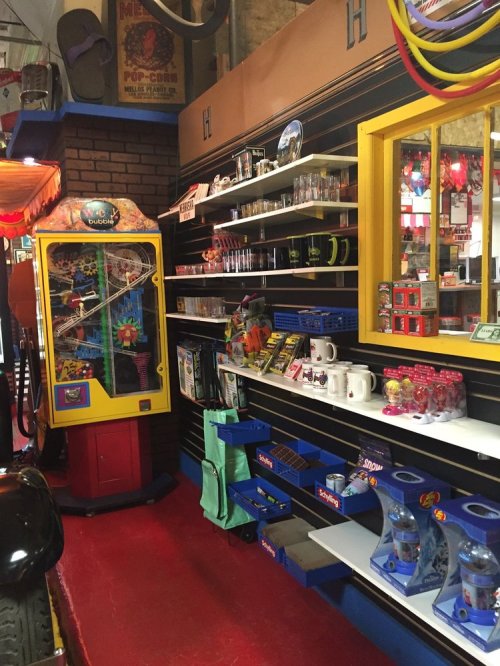 A colorful retro shop interior with shelves of toys, souvenirs, and a vintage arcade game machine.