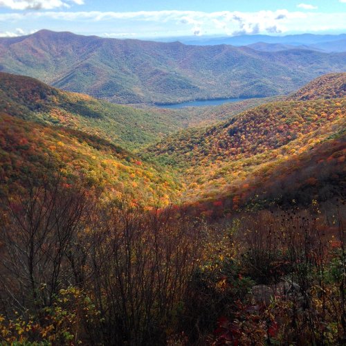 A scenic view of a colorful valley surrounded by mountains, showcasing autumn foliage and a serene lake.