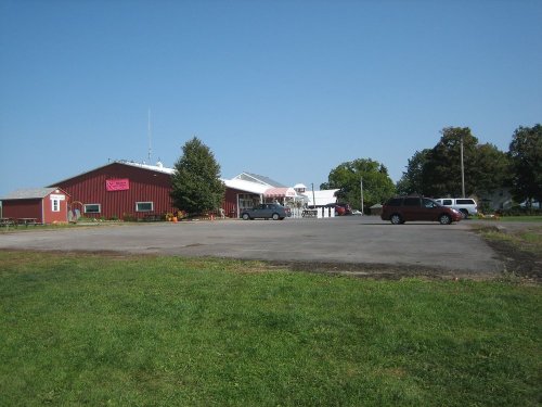 A red barn-style building with a parking lot and clear blue sky in the background. Green grass in the foreground.
