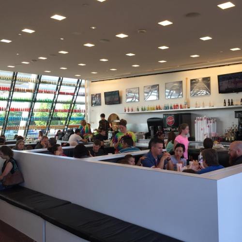 A modern restaurant interior with colorful decor, patrons dining, and a large window displaying vibrant bottles.