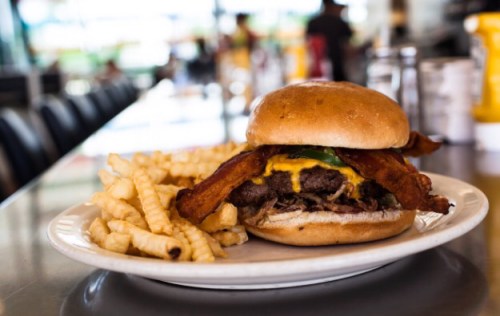 A juicy burger with bacon and cheese, served with crinkle-cut fries on a plate in a diner setting.