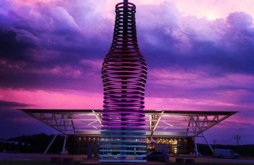 A colorful, spiraled sculpture stands against a dramatic sky with vibrant clouds at sunset.