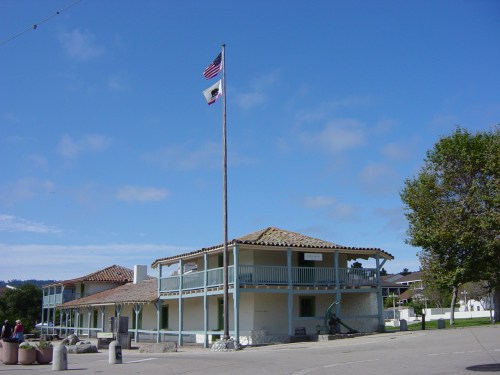 Historic building with a tiled roof, American and state flags flying, under a clear blue sky.