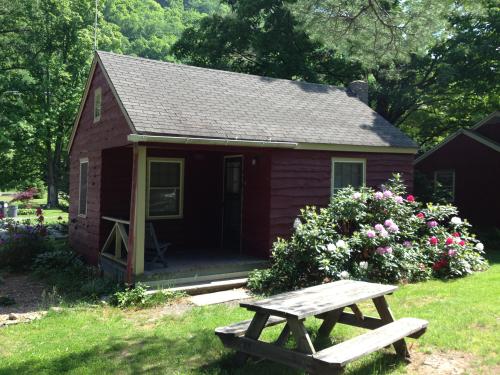 A small red cabin surrounded by greenery and flowers, with a picnic table in front on a sunny day.