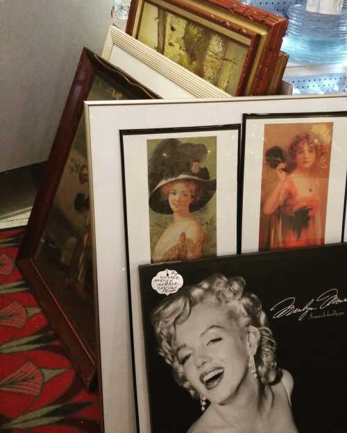 A collection of framed vintage artworks and photographs, including a portrait of a woman and a Marilyn Monroe print.