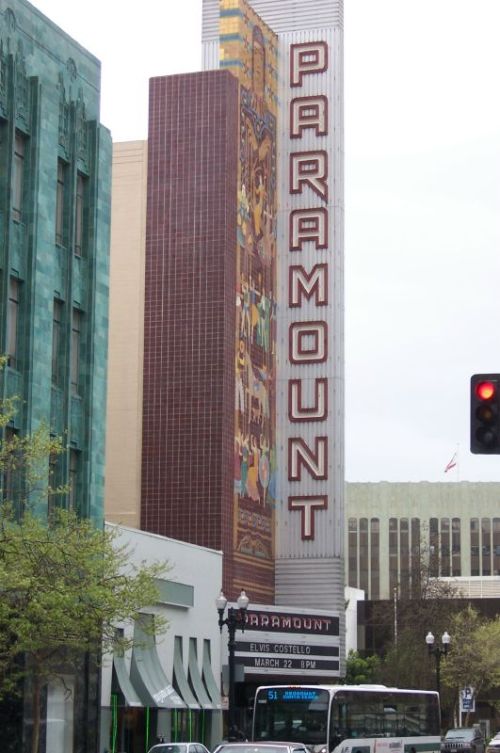 Signage of the Paramount Theatre, featuring colorful artwork and a tall marquee, set in an urban street scene.