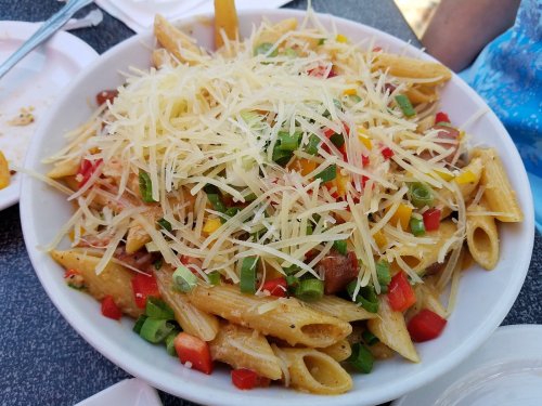 A large bowl of pasta topped with shredded cheese, diced peppers, and green onions.