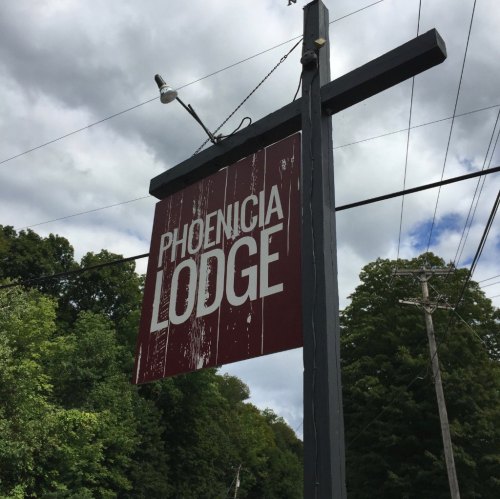Sign for Phoenicia Lodge against a cloudy sky, surrounded by trees and power lines.