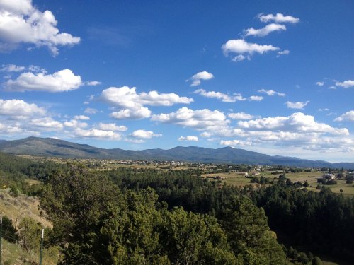 A scenic view of rolling hills and mountains under a blue sky with fluffy white clouds. Lush greenery in the foreground.