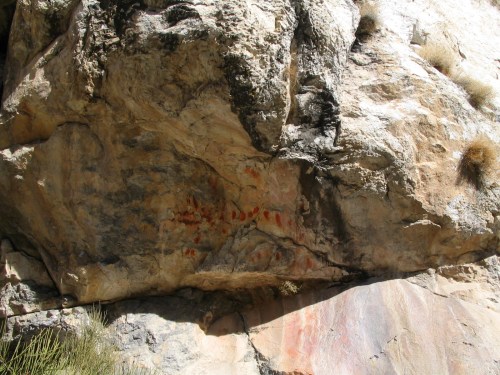 Ancient rock art featuring red handprints on a textured stone surface, surrounded by natural rock formations.